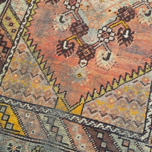 May include: A vintage rug with a geometric pattern in shades of orange, brown, yellow, and blue. The rug has a faded, worn look, giving it a unique character.
