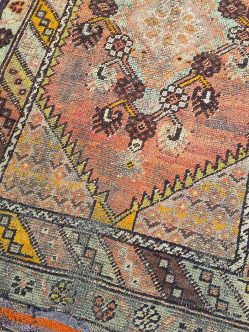 May include: A vintage rug with a geometric pattern in shades of orange, brown, yellow, and blue. The rug has a faded, worn look, giving it a unique character.