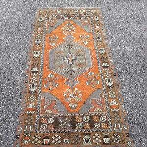 May include: A vintage Turkish rug with a geometric pattern in shades of orange, brown, and gray. The rug has a central medallion and a border with intricate designs.