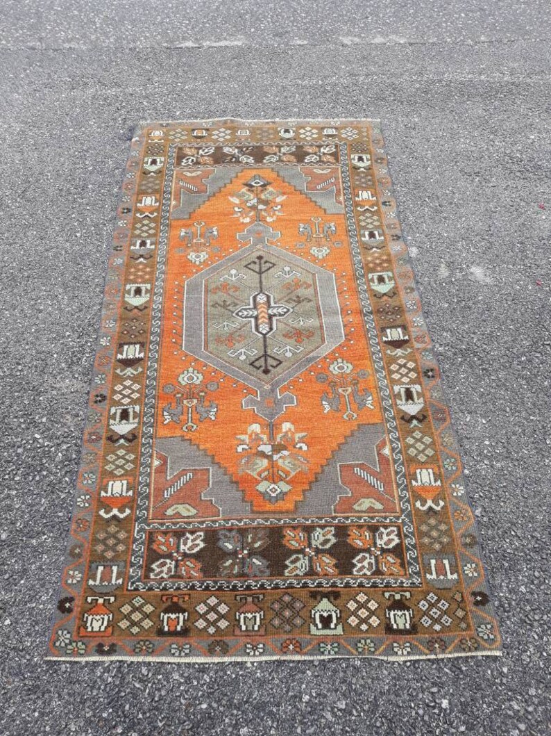May include: A vintage Turkish rug with a geometric pattern in shades of orange, brown, and gray. The rug has a central medallion and a border with intricate designs.