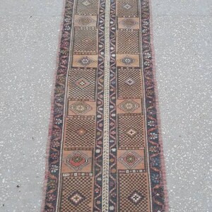 May include: A long, narrow rug with a traditional Turkish design. The rug is primarily brown with red, blue, and white accents. The rug has a fringe on both ends.