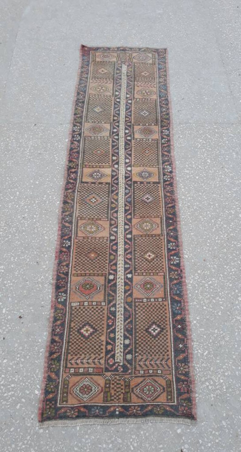 May include: A long, narrow rug with a traditional Turkish design. The rug is primarily brown with red, blue, and white accents. The rug has a fringe on both ends.