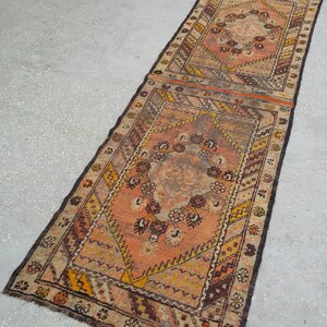 May include: A long, narrow rug with a traditional Persian design. The rug is made of wool and has a brown, orange, and cream color scheme. The rug has a fringe on both ends.