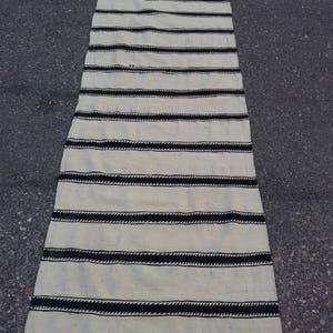 Pu&ograve; includere: Un tappeto a strisce bianche e nere con un design intrecciato. Il tappeto &egrave; fatto di fibre naturali e ha un aspetto rustico.