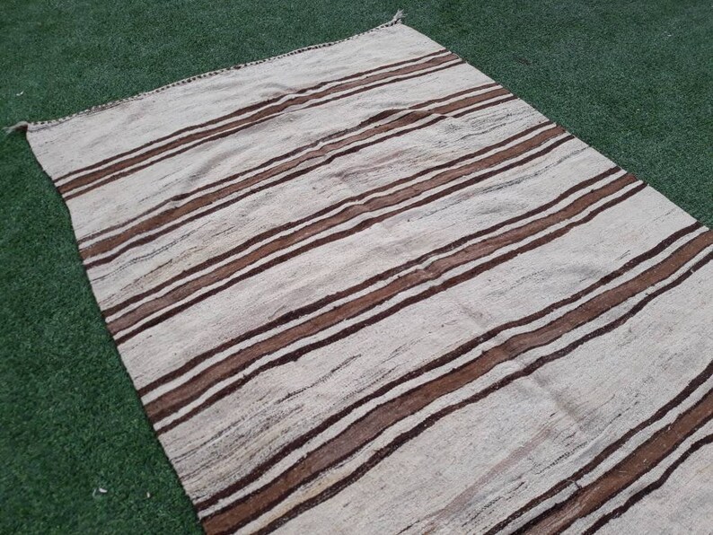 May include: A white and brown striped rug with a woven texture. The rug has a simple design with horizontal stripes.