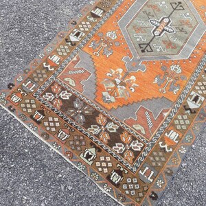 May include: A vintage Turkish rug with a geometric pattern in shades of orange, brown, gray, and white. The rug has a fringed edge and is made of wool.