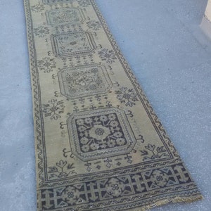 May include: A long, rectangular rug with a beige background and a black and white geometric pattern. The rug has a fringed edge.