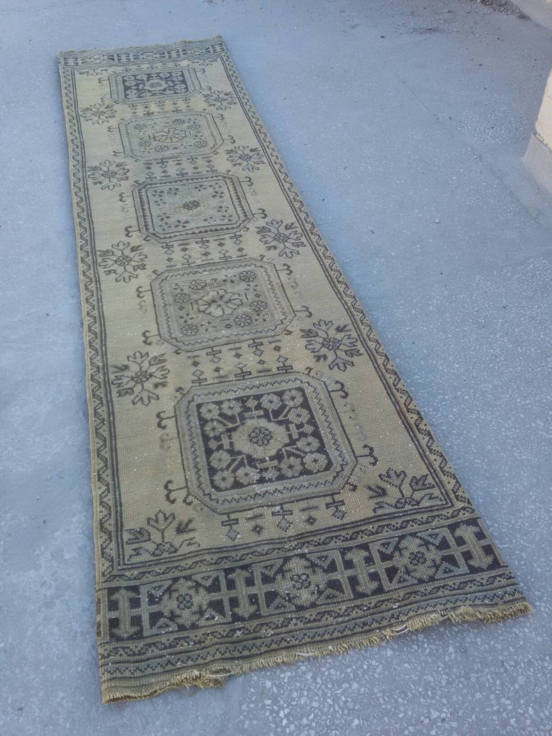 May include: A long, rectangular rug with a beige background and a black and white geometric pattern. The rug has a fringed edge.