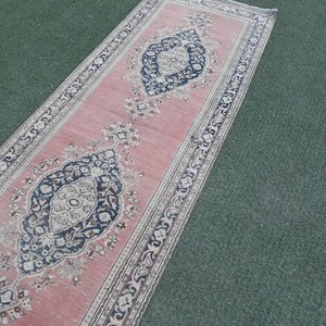 May include: A long, pink runner rug with a traditional Persian design. The rug has a central medallion with floral motifs and a border with repeating patterns.