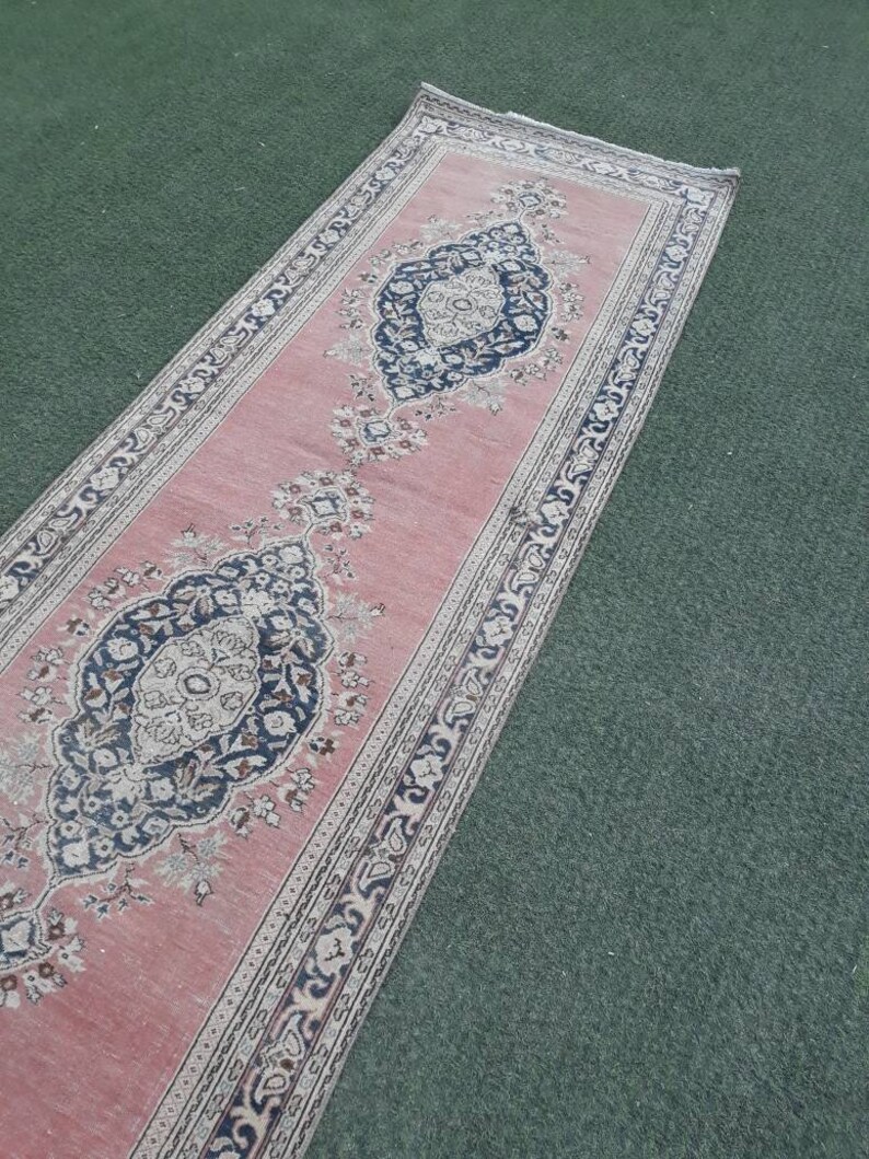 May include: A long, pink runner rug with a traditional Persian design. The rug has a central medallion with floral motifs and a border with repeating patterns.