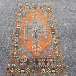 May include: A vintage Turkish rug with a geometric pattern in shades of orange, brown, and gray. The rug has a central medallion with a diamond shape and intricate details.