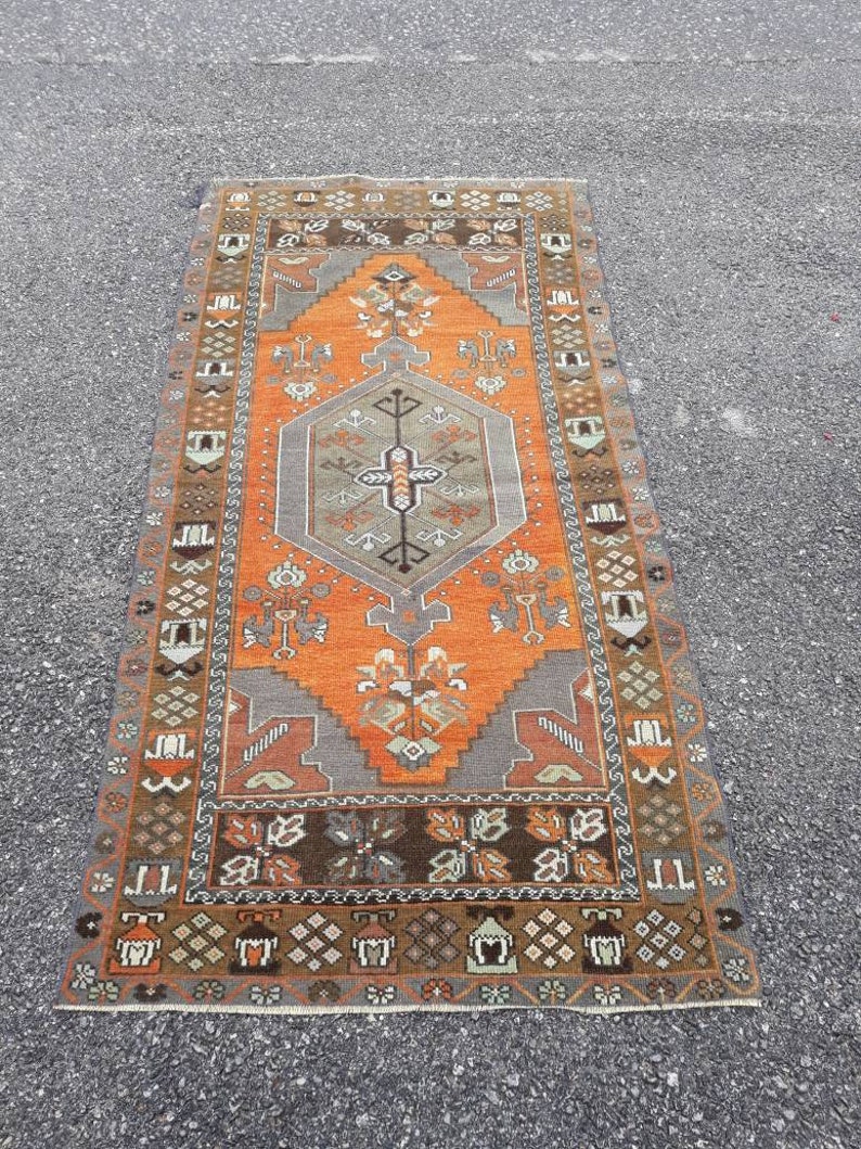 May include: A vintage Turkish rug with a geometric pattern in shades of orange, brown, and gray. The rug has a central medallion with a diamond shape and intricate details.
