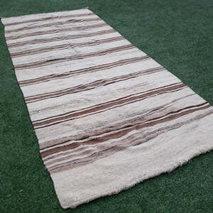 May include: A white and brown striped rug with a fringed edge. The rug is made of natural fibres and has a rustic, handwoven look.