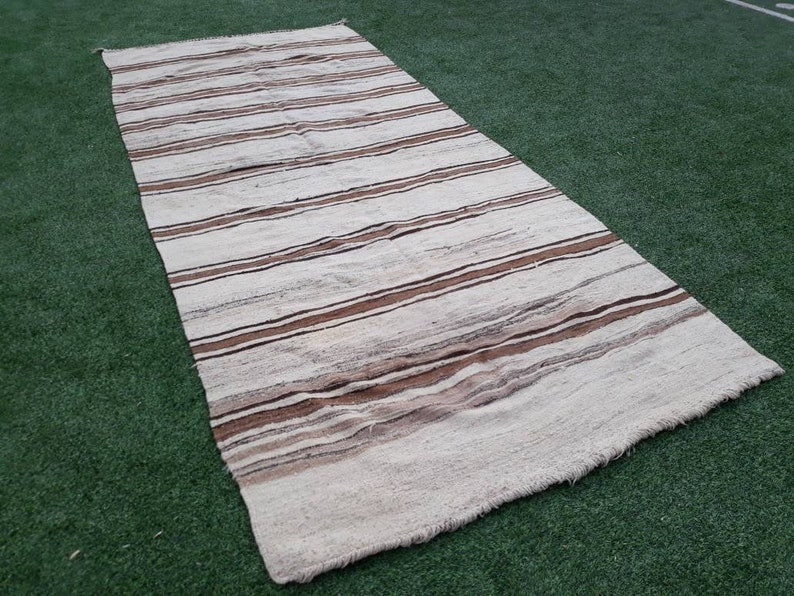 May include: A white and brown striped rug with a fringed edge. The rug is made of natural fibres and has a rustic, handwoven look.