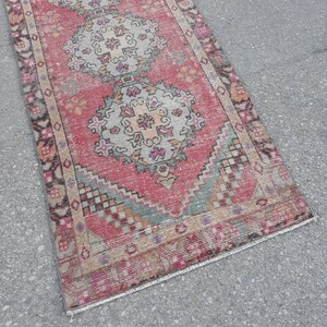May include: A vintage pink and cream runner rug with a traditional Persian design. The rug has a fringed edge and is made of wool.