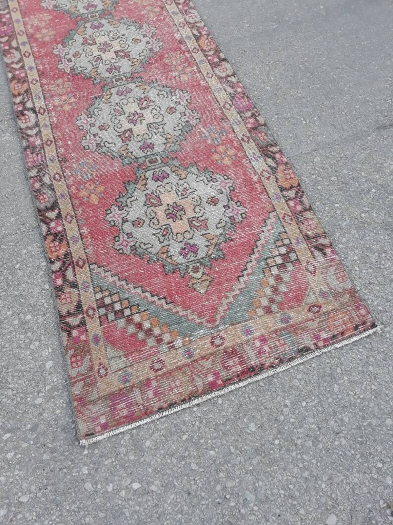 May include: A vintage pink and cream runner rug with a traditional Persian design. The rug has a fringed edge and is made of wool.