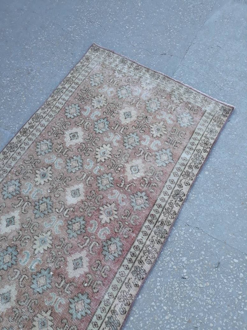 K&ouml;nnte beinhalten: Ein Vintage-L&auml;ufer mit einem verblassten rosa, cremefarbenen und blauen Blumenmuster. Der Teppich hat einen abgenutzten Look und ist perfekt, um Ihrem Zuhause einen Hauch von Boho-Stil zu verleihen.