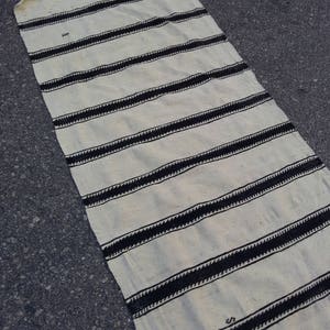 Pu&ograve; includere: Un tappeto a strisce bianche e nere con un design intrecciato. Il tappeto &egrave; realizzato in un materiale naturale morbido e ha un bordo con frange.
