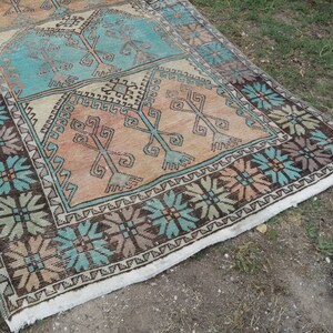 Puede incluir: Una alfombra turca vintage con un patr&oacute;n geom&eacute;trico en tonos marrones, turquesa y beige. La alfombra tiene un borde con flecos y est&aacute; hecha de lana.