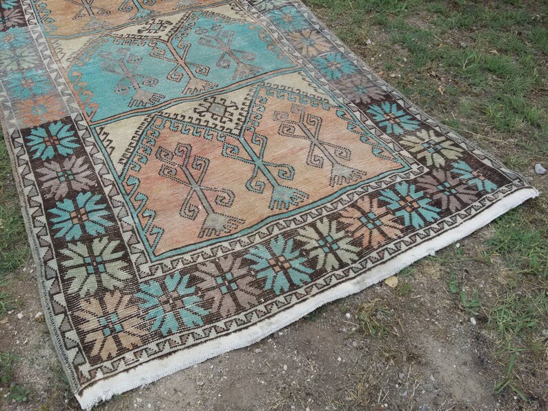 Puede incluir: Una alfombra turca vintage con un patr&oacute;n geom&eacute;trico en tonos marrones, turquesa y beige. La alfombra tiene un borde con flecos y est&aacute; hecha de lana.
