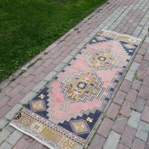 May include: A pink and blue patterned runner rug with a geometric design. The rug is laid out on a brick walkway.