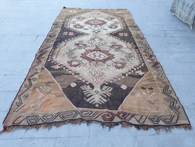 May include: A vintage Turkish rug with a brown, beige, and pink geometric pattern. The rug has a fringed edge and is made of wool.