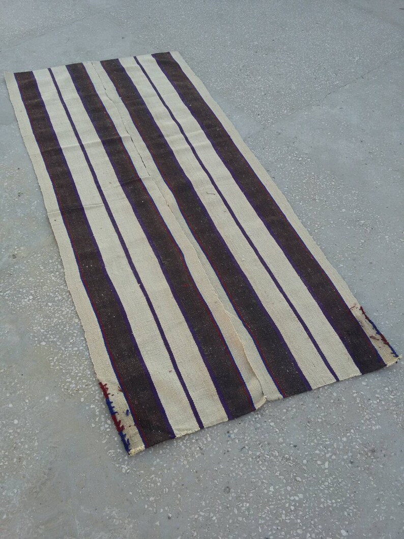 May include: A long, narrow, striped rug with alternating white and dark brown stripes. The rug is woven with a simple, rustic design and has a frayed edge.