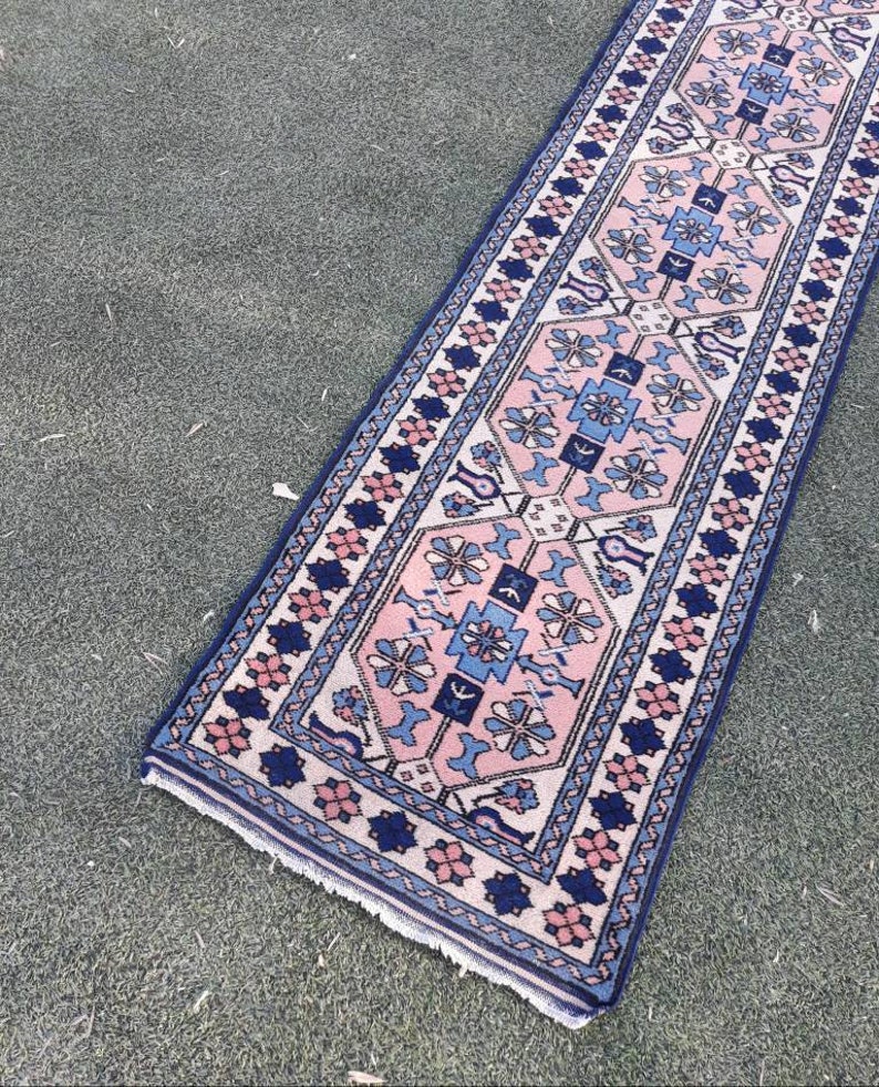 May include: A pink and blue patterned runner rug with a geometric design. The rug has a fringed edge and is made of wool.