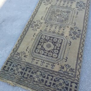 May include: A beige runner rug with a black and white geometric pattern. The rug has a fringe border and features a repeating design of squares with floral motifs.
