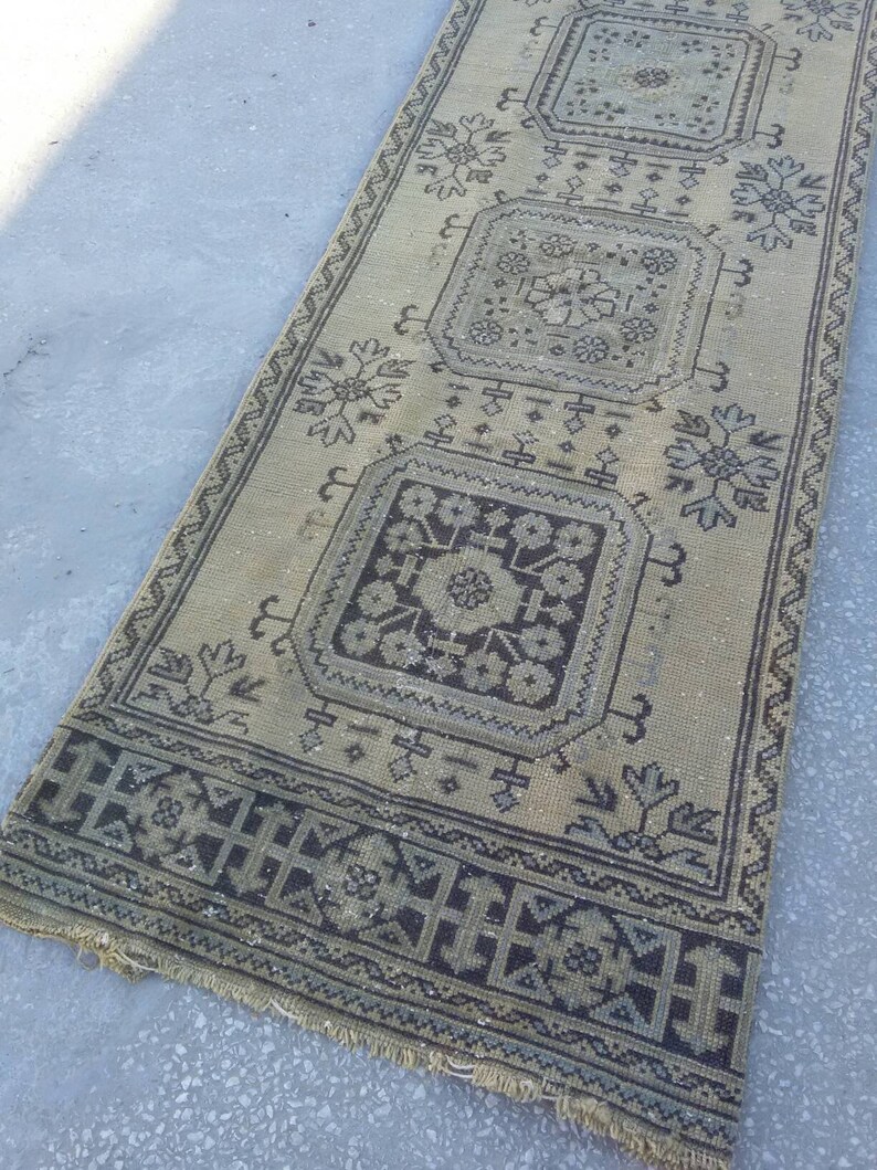 May include: A beige runner rug with a black and white geometric pattern. The rug has a fringe border and features a repeating design of squares with floral motifs.