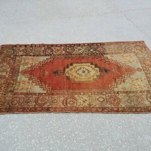 May include: A vintage Turkish rug with a red, beige, and brown geometric pattern. The rug has a faded, worn look, giving it a rustic and antique feel.