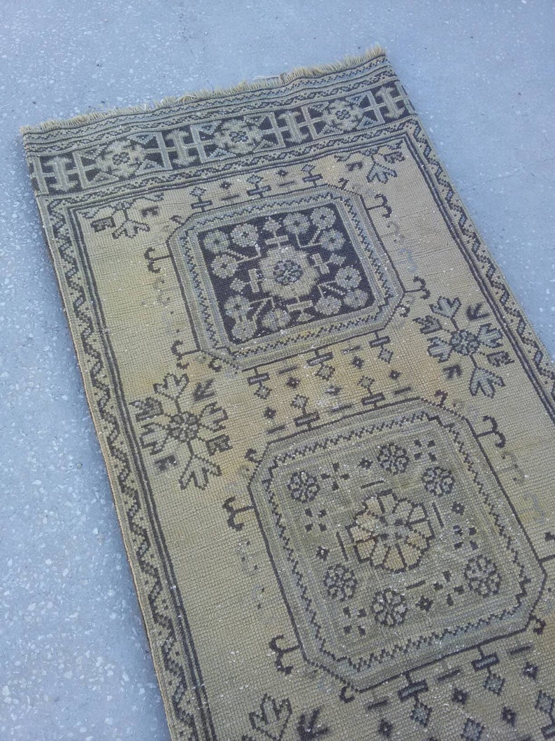 May include: A beige and brown patterned rug with a geometric design. The rug has a fringed edge and is made of a woven material.