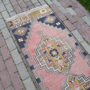 May include: A pink and yellow patterned runner rug with a geometric design. The rug has a black border and is made of a woven fabric.