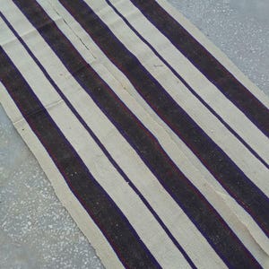 May include: A white and black striped rug with a red accent. The rug is woven with thick, textured yarn.