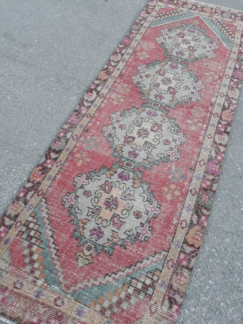 May include: A vintage Turkish runner rug with a faded pink background and intricate floral patterns in shades of beige, green, and brown. The rug has a distressed look and is perfect for adding a touch of bohemian charm to any room.