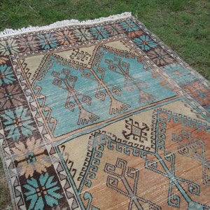 Puede incluir: Una alfombra turca vintage con un patr&oacute;n geom&eacute;trico en tonos azules, marrones y beige. La alfombra tiene un borde con flecos y est&aacute; tejida con un dise&ntilde;o tradicional.