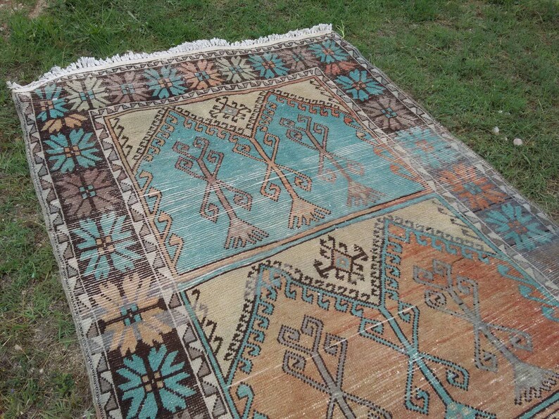 Puede incluir: Una alfombra turca vintage con un patr&oacute;n geom&eacute;trico en tonos azules, marrones y beige. La alfombra tiene un borde con flecos y est&aacute; tejida con un dise&ntilde;o tradicional.