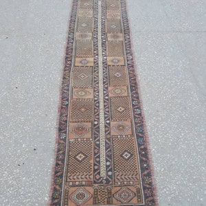 May include: A long, narrow rug with a traditional Persian design. The rug is primarily beige with brown, red, and black accents. The rug has a fringe border.