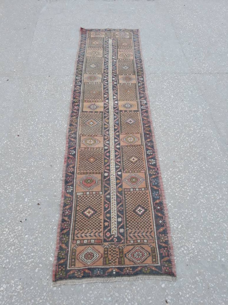 May include: A long, narrow rug with a traditional Persian design. The rug is primarily beige with brown, red, and black accents. The rug has a fringe border.