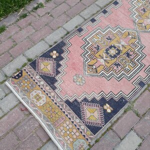 May include: A pink and yellow patterned rug with a dark blue border. The rug is laid out on a brick walkway.