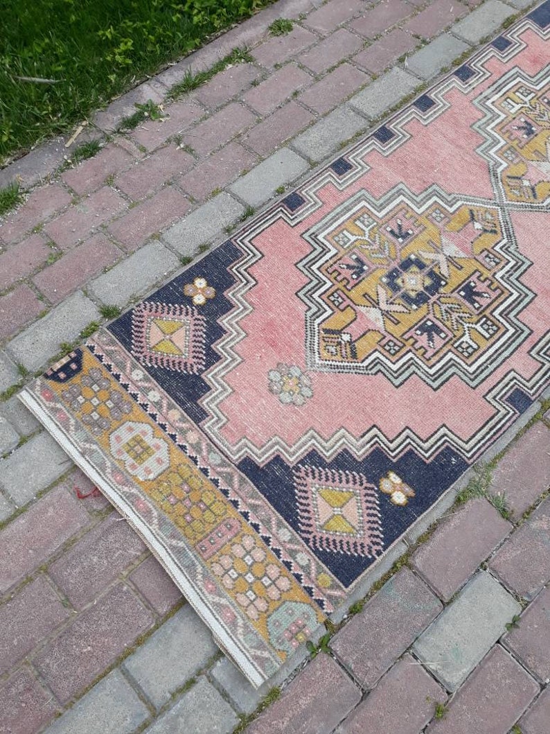 May include: A pink and yellow patterned rug with a dark blue border. The rug is laid out on a brick walkway.
