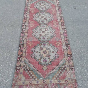 May include: A vintage pink and cream runner rug with a traditional floral pattern. The rug has a faded look and is made of wool.
