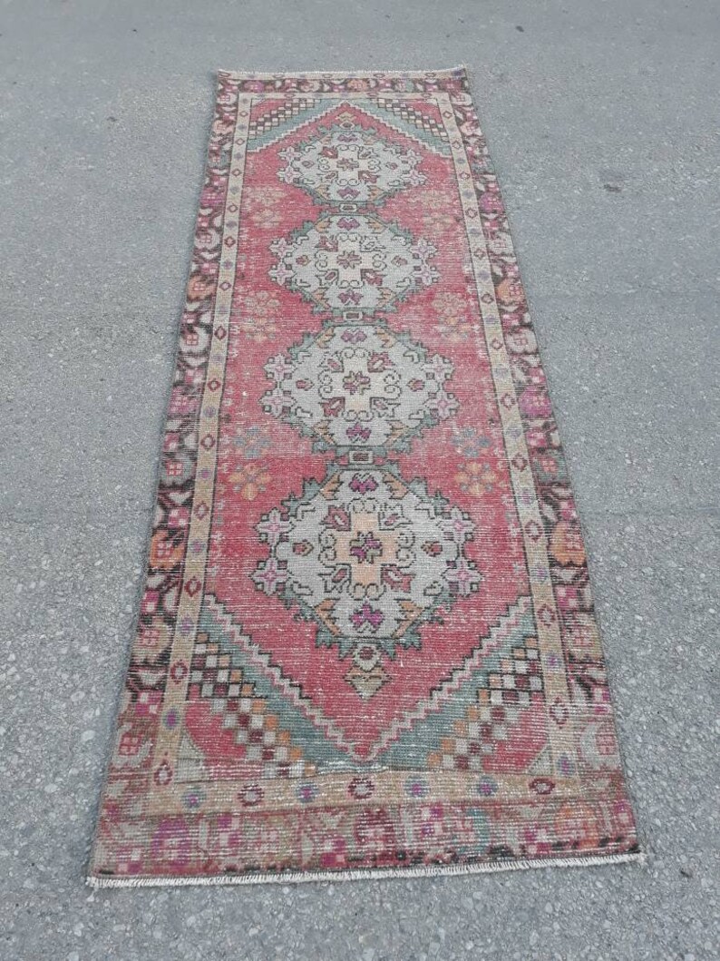 May include: A vintage pink and cream runner rug with a traditional floral pattern. The rug has a faded look and is made of wool.