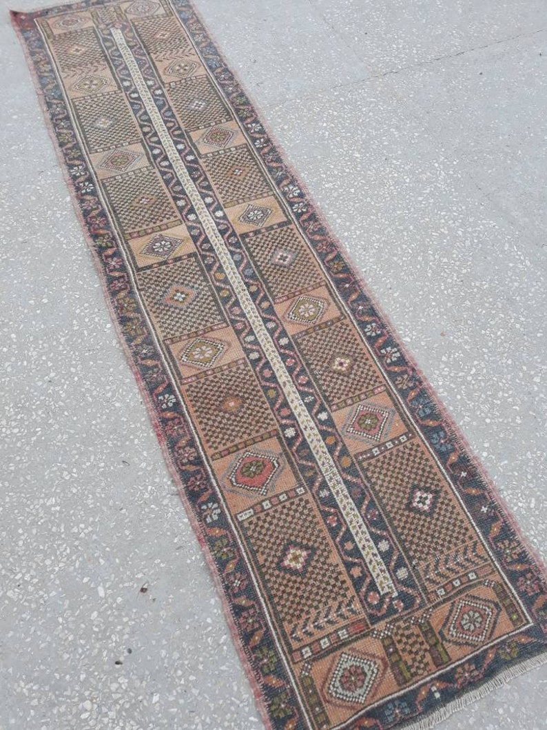 May include: A long, narrow rug with a traditional Persian design. The rug is made of wool and has a brown, beige, and red color scheme. The rug is in good condition and has a vintage look.