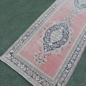 May include: A pink runner rug with a floral pattern and a dark blue border. The rug has a fringed edge.