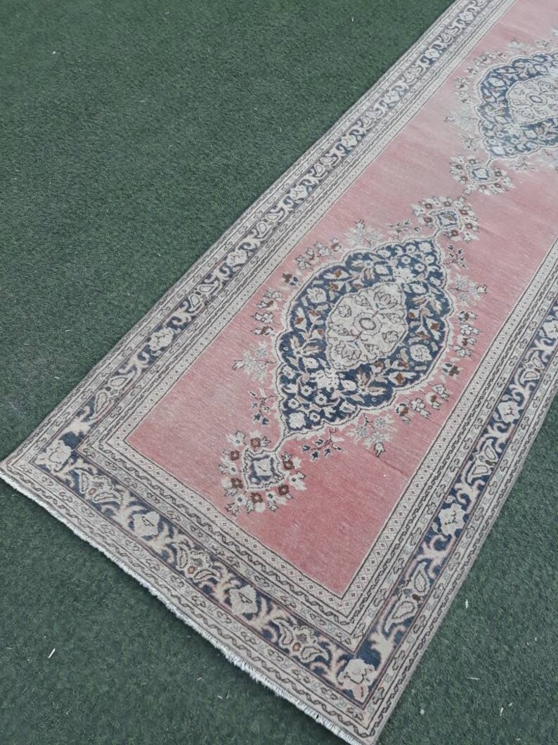 May include: A pink runner rug with a floral pattern and a dark blue border. The rug has a fringed edge.