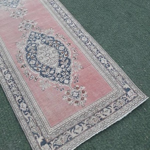 May include: A pink and cream runner rug with a floral pattern and a black and white border. The rug has a fringed edge.