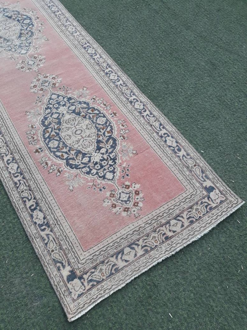 May include: A pink and cream runner rug with a floral pattern and a black and white border. The rug has a fringed edge.