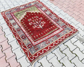 Peut inclure: Un tapis rouge, vert et rose à motifs avec un motif d'arbre au centre. Le tapis est posé sur une surface en béton gris.