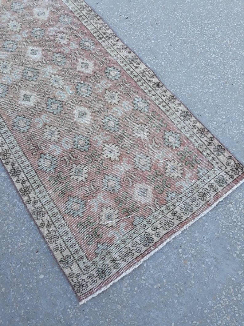 K&ouml;nnte beinhalten: Ein vintagefarbener L&auml;ufer in Rosa und Gr&uuml;n mit Fransen. Der L&auml;ufer hat ein florales Muster mit einem sich wiederholenden Design.